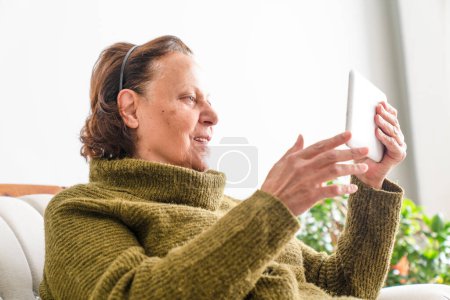 Foto de una mujer mayor feliz relajándose en el sofá con su tableta digital en casa
