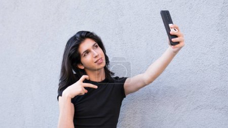 Téléchargez les photos : Une personne non binaire utilise un smartphone en plein air pour passer un appel vidéo - en image libre de droit