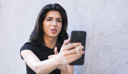 Téléchargez les photos : Une personne non binaire utilise un smartphone en plein air pour passer un appel vidéo - en image libre de droit