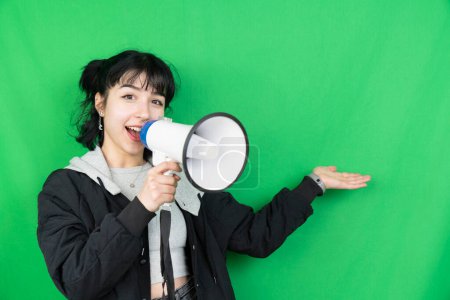 Foto de Recortado disparo de una mujer joven sosteniendo un megáfono mientras posando sobre un fondo verde - Imagen libre de derechos