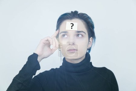 Photo for Focused woman with question mark paper sticker on forehead in studio. - Royalty Free Image