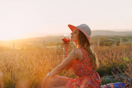 Téléchargez les photos : Femme profitant du coucher de soleil d'été au champ de fleurs de lavande avec un verre de vin - en image libre de droit