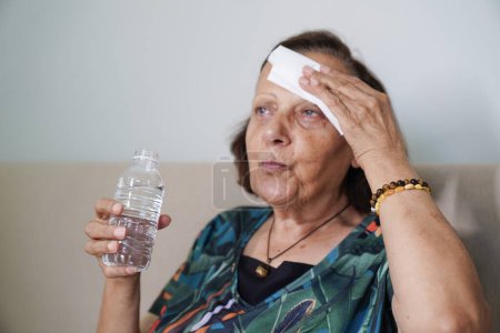 Téléchargez les photos : Femme âgée transpiration souffrance coup de chaleur à la maison - en image libre de droit