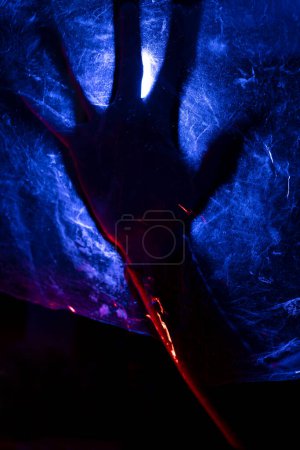 Foto de Brazo de mujer presionando contra la cortina. mujer silueta detrás de la luz azul plantea misteriosa y artísticamente - Imagen libre de derechos