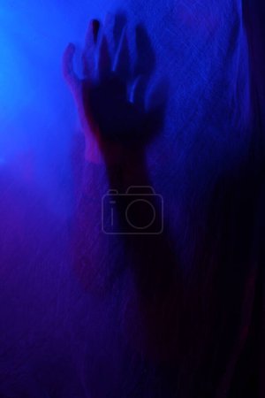 Téléchargez les photos : Bras de femme pressant contre le rideau. silhouette femme derrière la lumière bleue pose mystérieusement et artistiquement - en image libre de droit