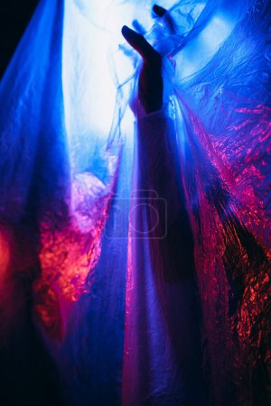 Photo for Arm of woman pressing against curtain. silhouette woman behind blue light poses mysteriously and artistically - Royalty Free Image
