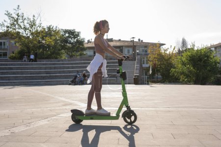 Téléchargez les photos : Femme équitation e-scooter à travers la ville - en image libre de droit