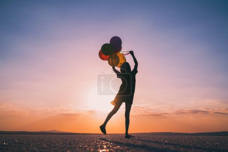 Foto de Silueta de mujer sosteniendo globos mientras está de pie en la playa contra el cielo durante el atardecer - Imagen libre de derechos