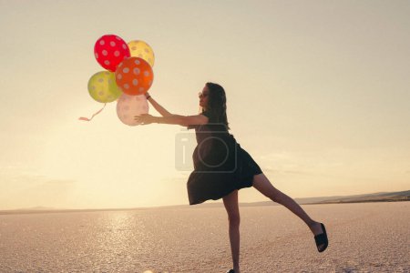 Photo for Silhouette of woman holding balloons while standing at beach against sky during sunset - Royalty Free Image