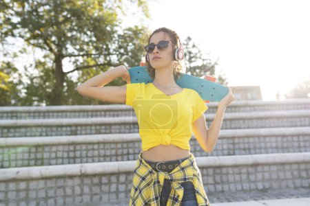 Téléchargez les photos : Jeune femme moderne en plein air dans la ville avec skateboard - en image libre de droit