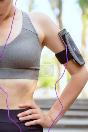 Foto de Atleta femenina que usa ropa deportiva y usa un teléfono inteligente para escuchar música - Imagen libre de derechos