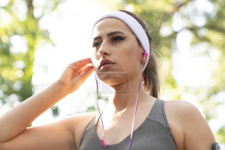 Photo for Young fitness sports woman running in the park. Happy athletic woman listening music on earphones while running in nature in the morning. - Royalty Free Image