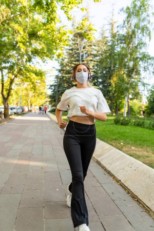 Téléchargez les photos : Jeune femme portant un masque facial courant dans le parc - en image libre de droit