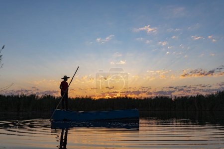 Téléchargez les photos : Pêcheur local ramant un bateau sur une rivière aux petites heures du matin. personne en petit bateau en bois sur mer calme - en image libre de droit