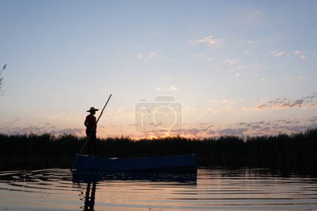 Photo for Local fisherman rowing a boat on a river in the early morning hours. person in small wooden boat on calm sea - Royalty Free Image