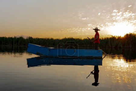 Foto de Pescador local remando un barco en un río en las primeras horas de la mañana. persona en pequeño barco de madera en el mar tranquilo - Imagen libre de derechos