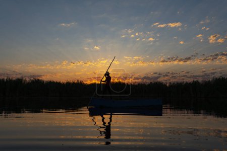 Téléchargez les photos : Pêcheur local ramant un bateau sur une rivière aux petites heures du matin. personne en petit bateau en bois sur mer calme - en image libre de droit