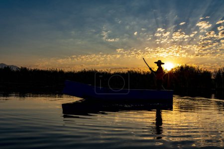 Foto de Pescador local remando un barco en un río en las primeras horas de la mañana. persona en pequeño barco de madera en el mar tranquilo - Imagen libre de derechos