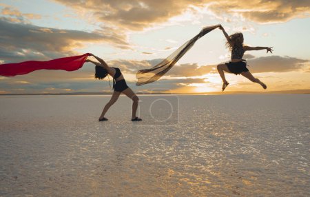 Foto de Dos mujeres bailan con gracia en la playa junto al mar en un día de verano - Imagen libre de derechos
