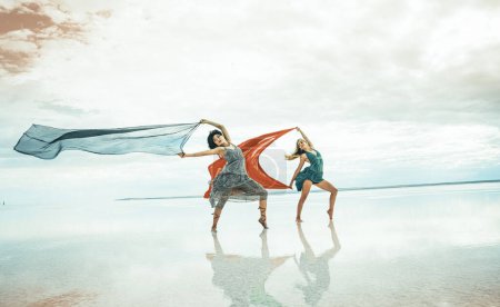 Photo for Two women gracefully dances on the beach by the sea on a summer day - Royalty Free Image
