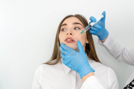 Téléchargez les photos : Photo de belle femme recevant un traitement de mésothérapie au visage par un spécialiste en gants dans un salon de beauté - en image libre de droit