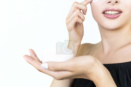 Foto de Hermosa mujer joven sosteniendo tarro y aplicando crema facial, aislado sobre fondo blanco - Imagen libre de derechos