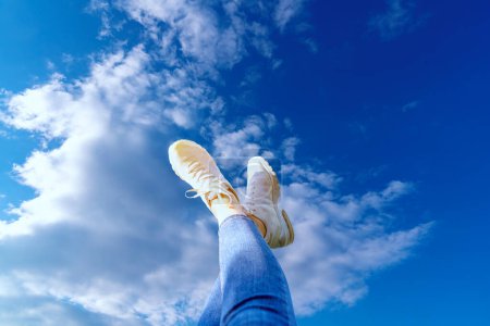 Photo for Legs in white sneakers and jeans against sky with lush clouds - Royalty Free Image