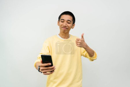 Foto de Joven asiático hombre con smartphone mostrando pulgares arriba en blanco estudio - Imagen libre de derechos