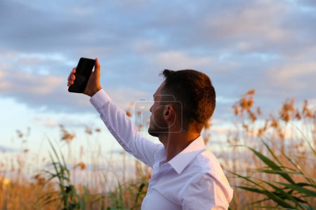 Photo for Man taking pictures by phone with sunset sky background - Royalty Free Image