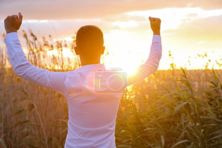 Photo for Young man in white shirt with raised hands  in the field,back view - Royalty Free Image