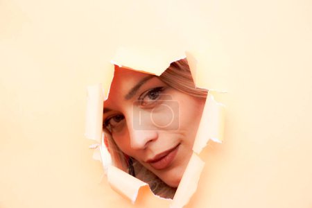 Photo for A woman's face is partially visible through a hole in a piece of paper. Concept of mystery and advert, as the viewer is left to wonder what the woman's face looks like and what she is thinking - Royalty Free Image