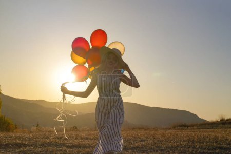 Téléchargez les photos : Jeune femme heureuse avec des ballons au coucher du soleil en été. Femme heureuse courir et s'amuser avec des ballons dans la nature au coucher du soleil - en image libre de droit