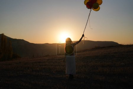 Téléchargez les photos : Jeune femme heureuse avec des ballons au coucher du soleil en été. Femme heureuse courir et s'amuser avec des ballons dans la nature au coucher du soleil - en image libre de droit