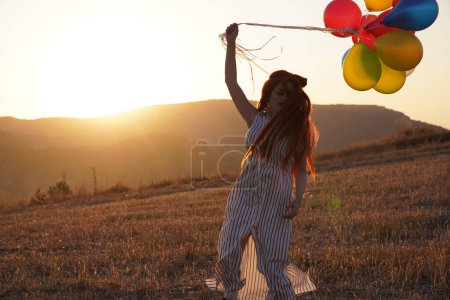 Photo for Young happy woman with balloons at sunset in summer. Happy woman running and having fun with balloons in nature at sunset - Royalty Free Image