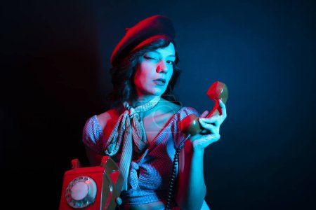 Téléchargez les photos : Jeune femme parlant sur Orange téléphone rétro. Haute Femme modèle de mode dans les lumières lumineuses colorées bleu néon et violet posant en studio. - en image libre de droit