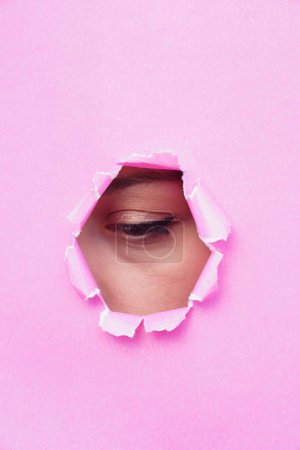 Foto de Un ojo de mujer mirando a través de papel rosa roto. espacio de copia para texto - Imagen libre de derechos