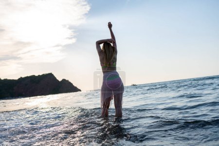 Téléchargez les photos : Femme heureuse marchant sur la plage au coucher du soleil.Belle femme heureuse se détendre marchant sur la plage près de la mer lorsque le coucher du soleil dans la soirée. Lifestyle femme voyage sur la plage concept. - en image libre de droit