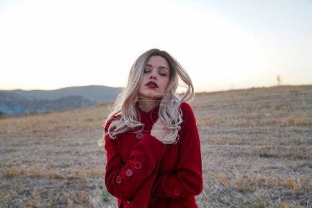 Foto de Una mujer rubia con ropa roja está de pie en un campo. Retrato emocional y estético de una hermosa mujer rubia - Imagen libre de derechos