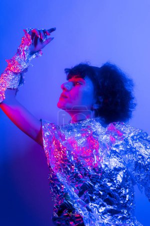 Téléchargez les photos : Haute Femme modèle de mode dans les lumières lumineuses colorées bleu néon et violet posant en studio. Portrait de belle femme avec maquillage rayonnant à la mode. Art design style vif - en image libre de droit