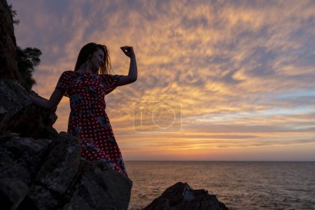 Photo for Silhouette of a lonely woman sitting on the rocks. A lonely woman watching the sea at sunset - Royalty Free Image