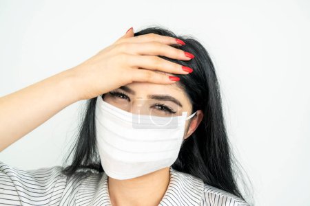 Foto de Mujer joven con máscara quirúrgica en la cara contra SARS-CoV-2. COVID-19 Pandemic Coronavirus Chica joven en habitación blanca con máscara facial - Imagen libre de derechos