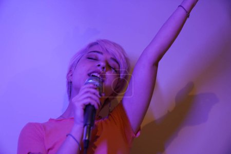 Foto de Una mujer cantando en un micrófono con pelo rosa. joven mujer canta con entusiasmo y juguetón - Imagen libre de derechos
