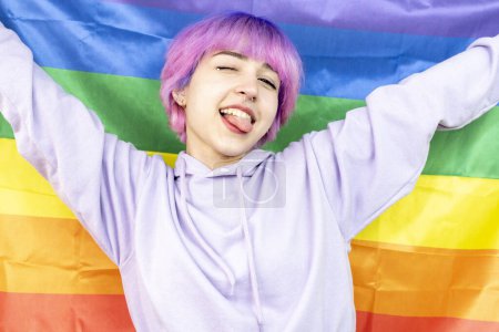 Photo for A woman with pink hair is holding a rainbow flag. She is smiling and she is happy. LGBT young woman holding LGBT flag on white background - Royalty Free Image