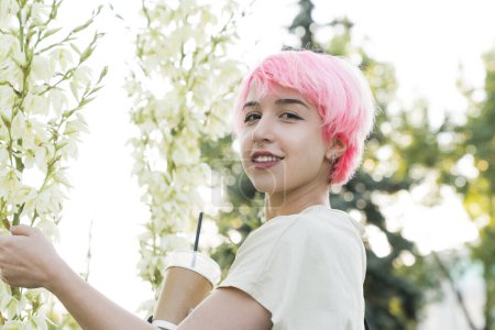 Téléchargez les photos : Une jeune femme aux cheveux roses et au chapeau noir tient une tasse de café et profite du printemps dans le parc - en image libre de droit