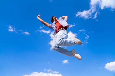 Foto de Un hombre está saltando en el aire con los brazos extendidos. El cielo es azul y hay nubes en el fondo. La escena es alegre y enérgica - Imagen libre de derechos