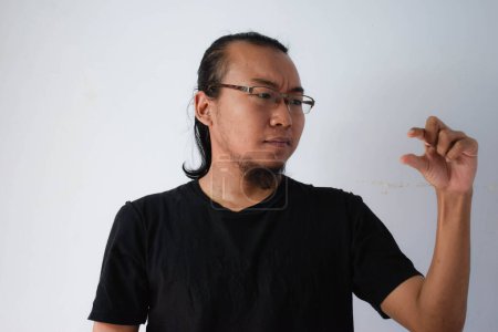 Foto de Hombre asiático adulto vistiendo camiseta negra y gafas con pelo largo Mostrando signo de mano pellizco en fondo gris. - Imagen libre de derechos