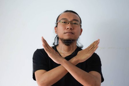 Photo for Adult Asian man wearing black t-shirt and eyeglasses with long hair Showing crossed hand in grey background. - Royalty Free Image