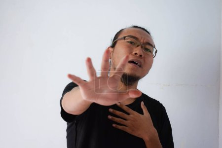 Foto de Adulto asiático hombre usando negro camiseta y gafas con el pelo largo tiene ataque al corazón en gris fondo. - Imagen libre de derechos