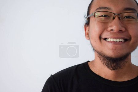 Foto de Adulto asiático hombre vistiendo camiseta negra y gafas con el pelo largo haciendo sonriendo a la cámara en fondo gris. - Imagen libre de derechos