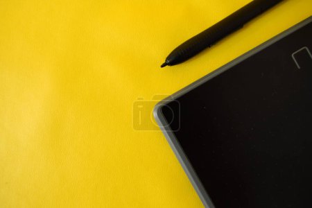 Téléchargez les photos : Pose plate de la tablette de stylo créatif graphique recadrée, avec espace de copie sur fond jaune - en image libre de droit